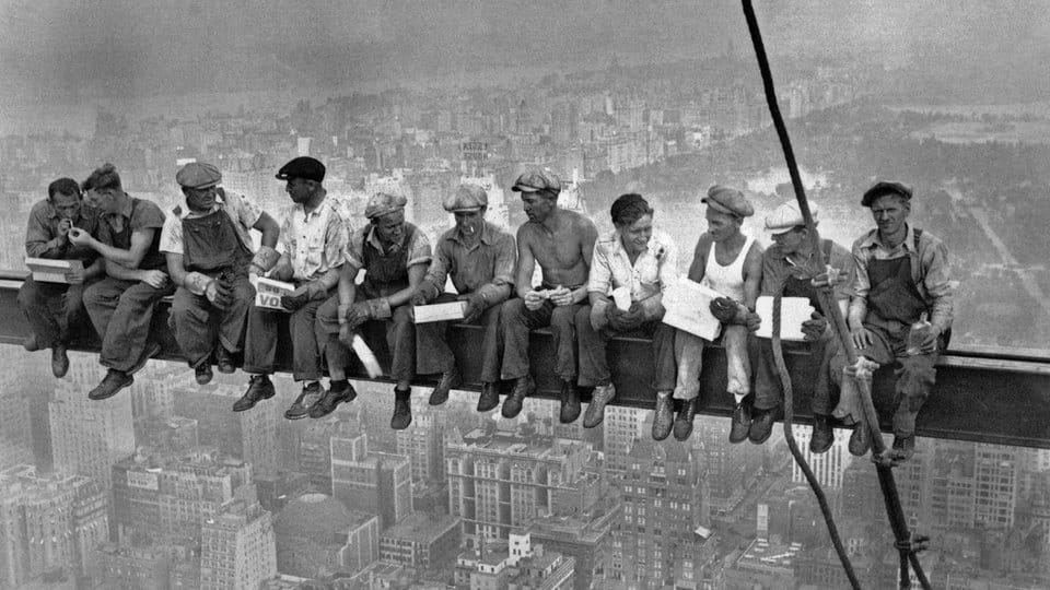 Historisches Foto von Bauarbeitern, die auf einem Stahlträger in schwindelerregender Höhe ihre Mittagspause machen.“