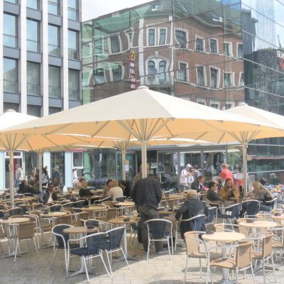 Cremefarbene Großschirme auf einem belebten Platz vor einem modernen Gebäude, ideal für Gastronomie und Außengastronomie.