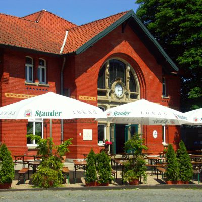 Weiße Sonnenschirme mit Stauder- und Lukas-Werbedruck vor einem historischen Backsteingebäude, ideal für Gastronomie und Brauereien.